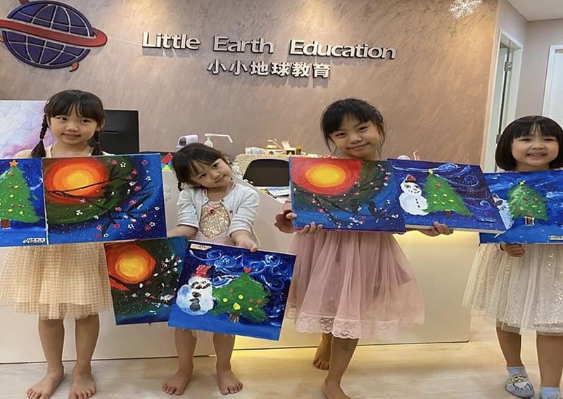 Four girls hold up their paintings of Christmas trees, snowmen and a glowing sun