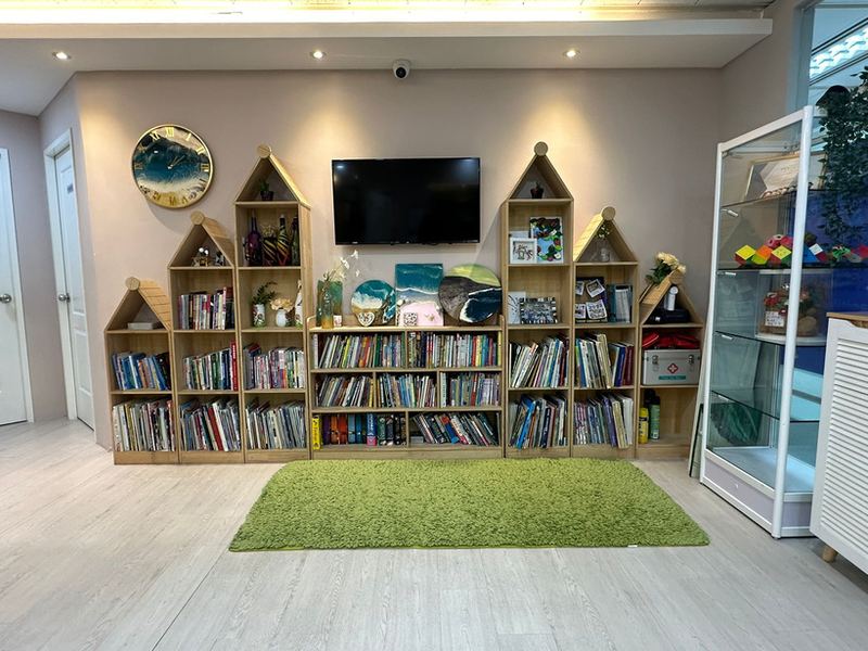 The centre's reading corner: house-shaped wooden bookshelves full of children's books, a television on the wall and a green rug on the floor